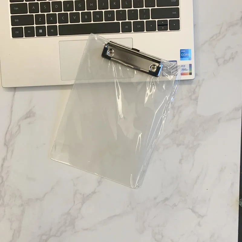 Transparent A4 plastic plate holder with metal clip, holding white paper, on a desk.