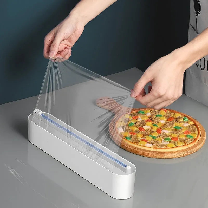 Black plastic cling film cutter and dispenser unit mounted on a refrigerator door.