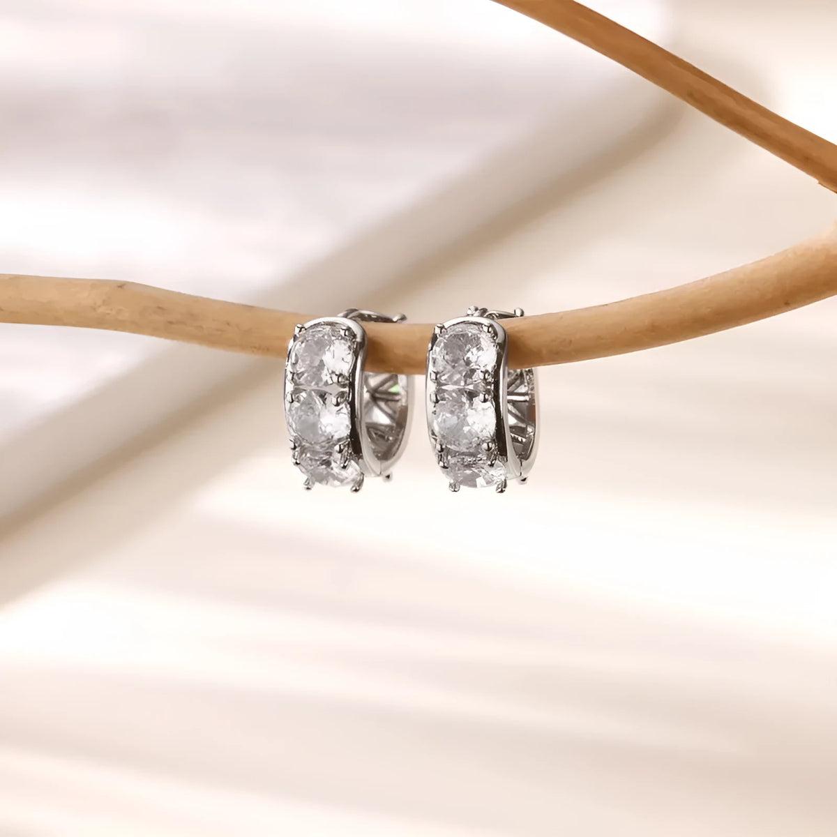 A pair of polished stainless steel U-shaped clip-on earrings with small inlaid zircon stones on a white background.
