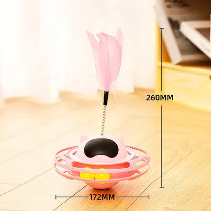 Pink self-hi tumbler cat toy with plush element on a turntable base, next to a play stick.