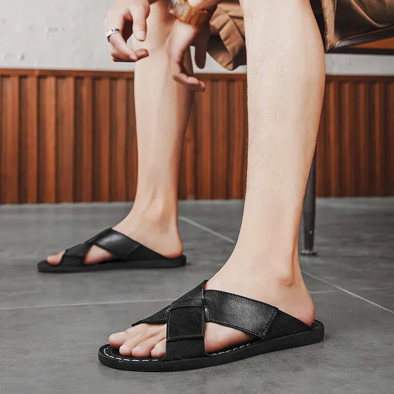 Men's black frosted pigskin leather slip-on sandals with a sewn rubber sole on a beach background.