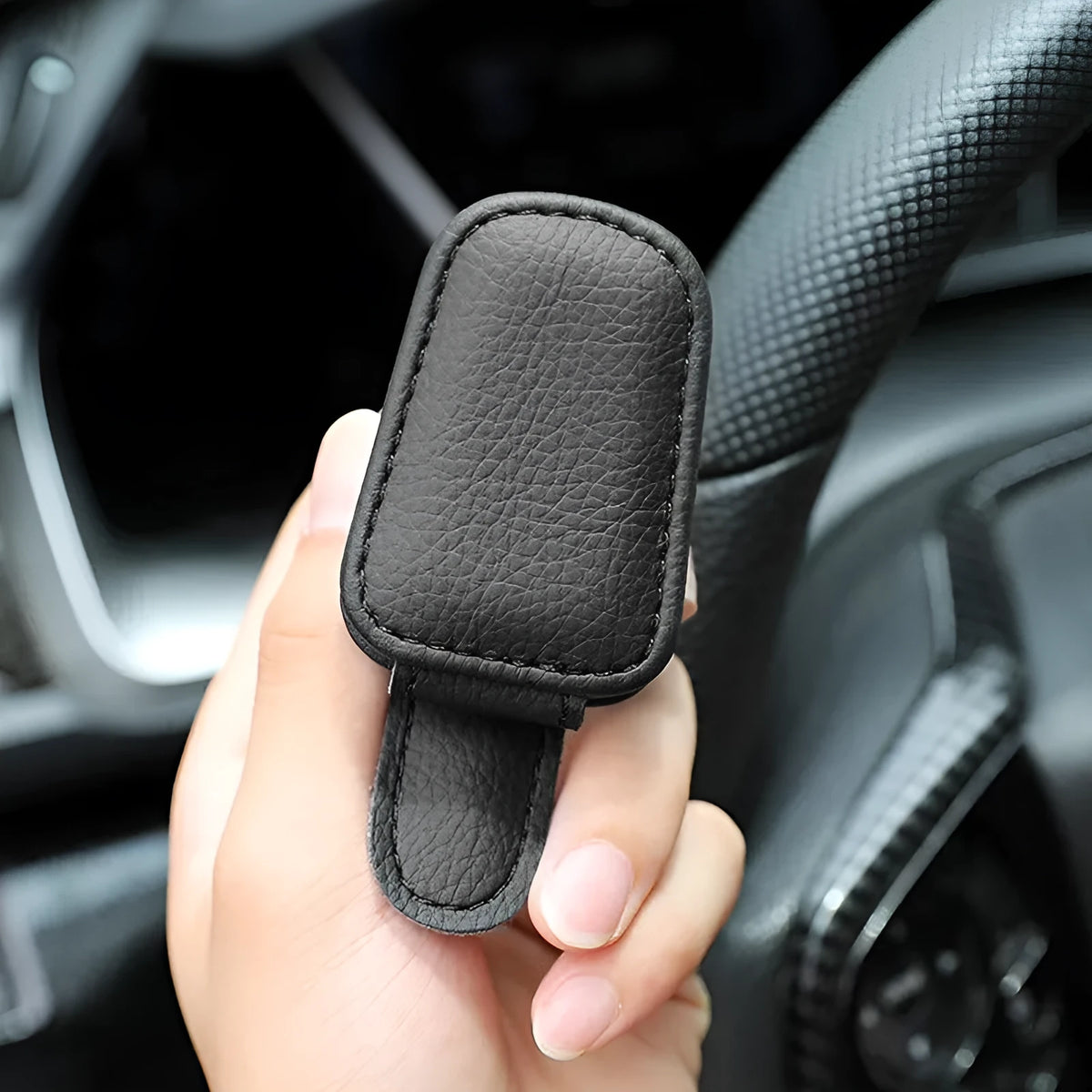 Car sunglasses holder clip with PU leather case attached to a sun visor.