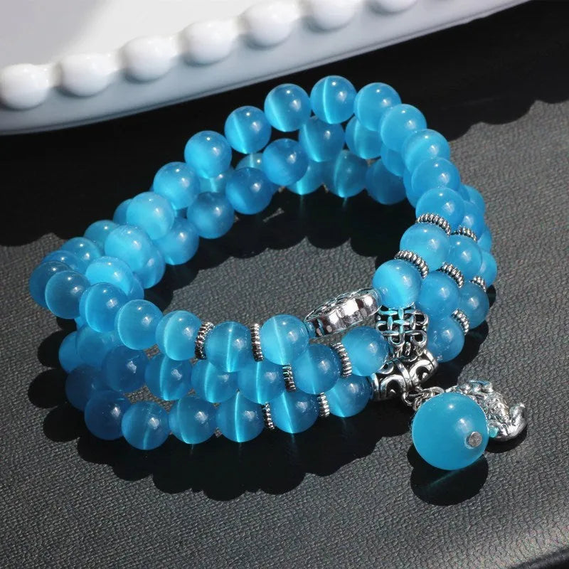 Close-up of a women's opal cat eye bracelet with three geometric rings and a lucky cat charm on a long, adjustable cord.