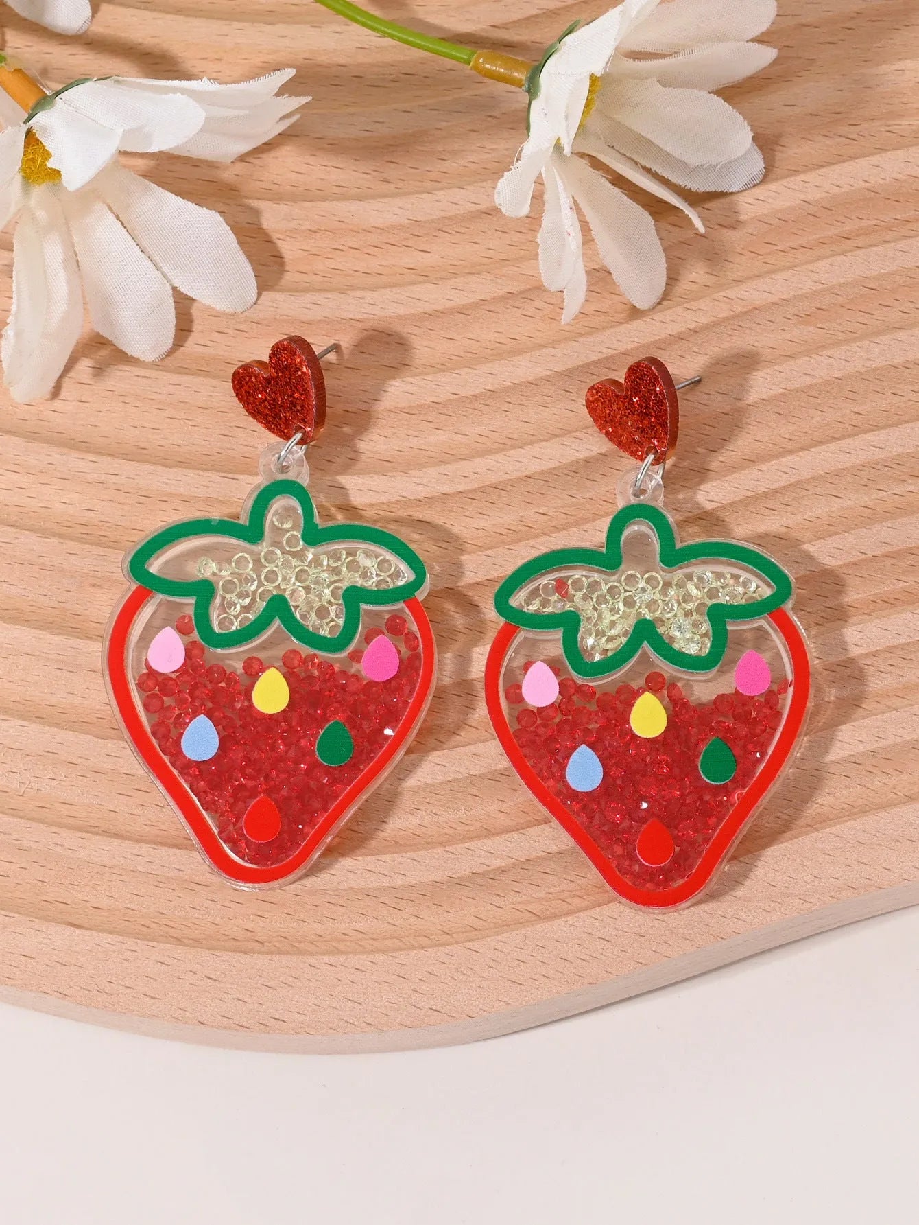 A pair of colourful acrylic earrings shaped like a strawberry and a cherry on a woman's ear.