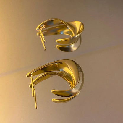 A pair of gold twisted geometric metal earrings with a round detail on a white background.