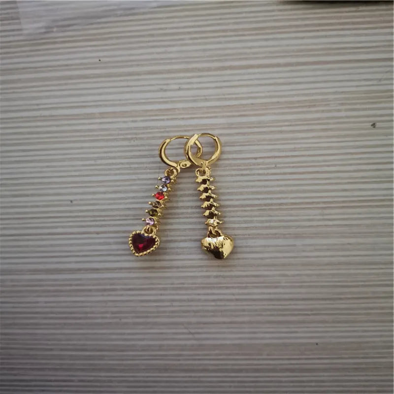 A pair of small gold-coloured heart-shaped alloy earrings on a plain background.