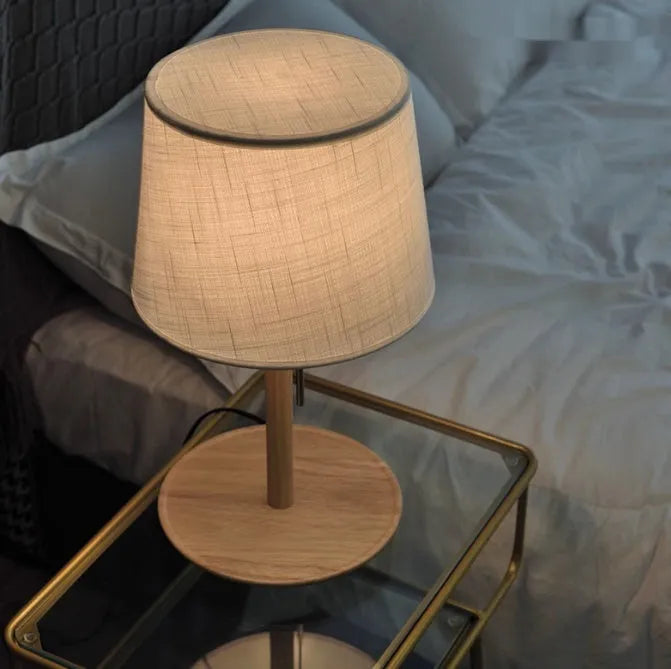 Walnut coloured solid wood bedside lamp with white fabric shade and cable switch.