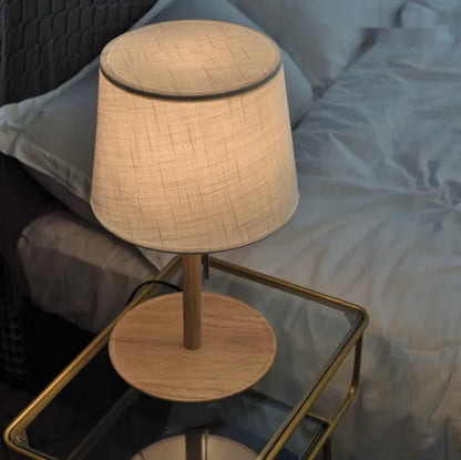 Walnut coloured solid wood bedside lamp with white fabric shade and cable switch.