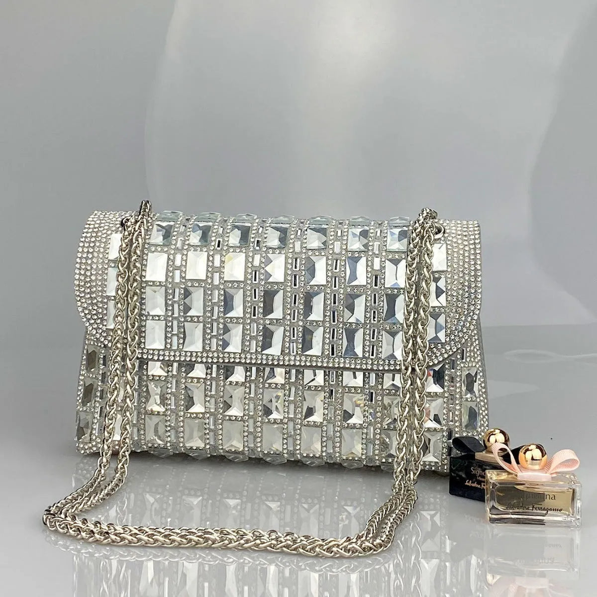 Silver rhinestone-decorated PU leather clutch bag with a metal chain strap, shown open to reveal interior phone pocket.