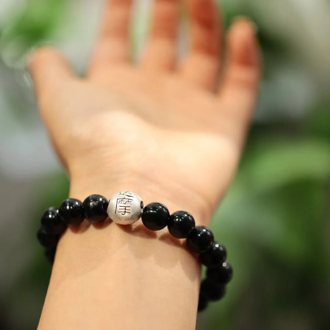 Close-up of a women's black agate bracelet with 10mm beads and a sterling silver clasp on a wrist.