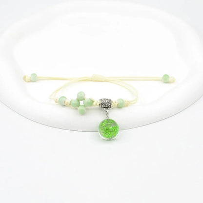 Close-up of a hand-woven bracelet with a large 1.4cm glass bead containing colourful dried flowers.