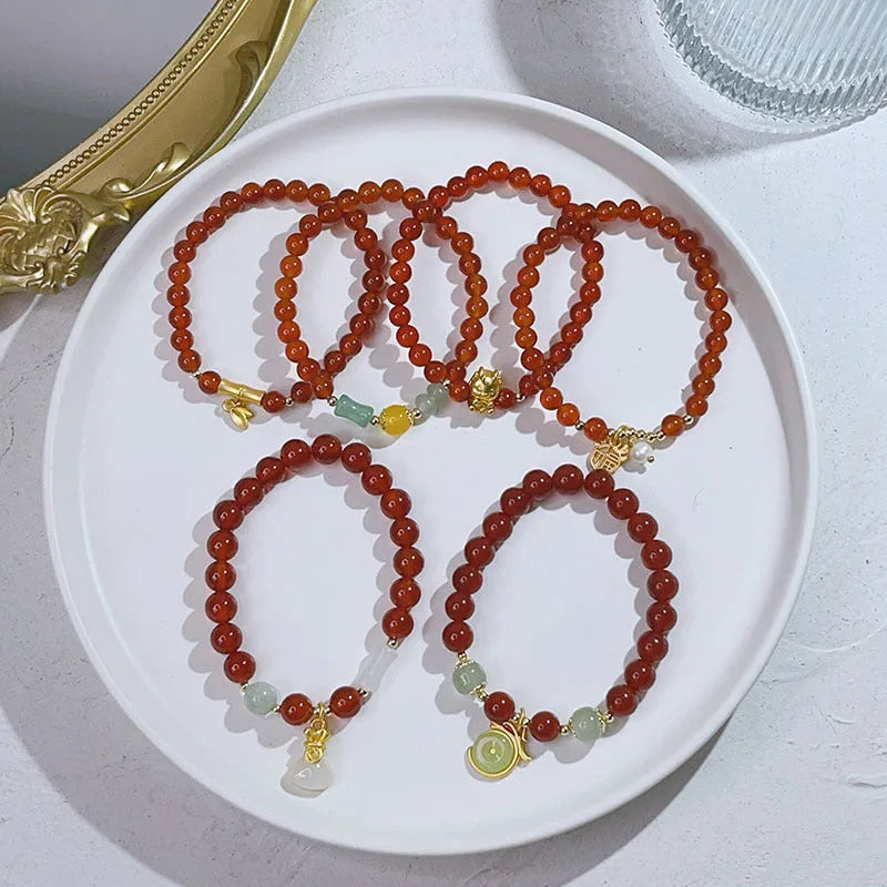 Close-up of a red agate bracelet with a dragon charm and Lucky Bag symbol on a wrist.