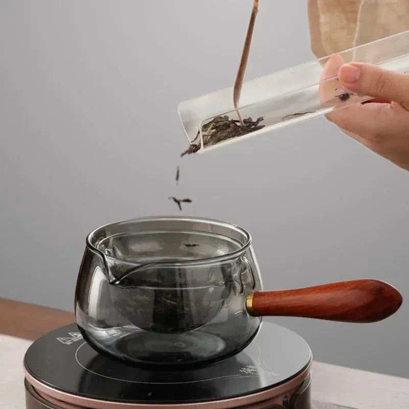 Transparent borosilicate glass rotary teapot with wooden handle and built-in infuser on a wooden surface