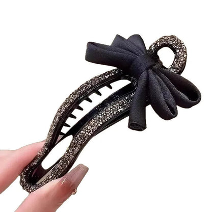 A black crystal bow on a clear 11.5cm long acrylic banana hair clip with bobby pin back.