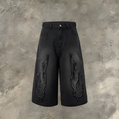 Men's black cropped denim shorts with a red and yellow flame embroidery patch on the leg.