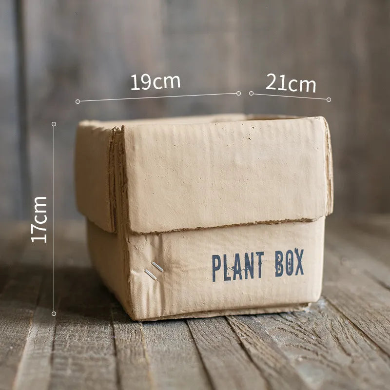 A grey cement flowerpot with a folded paper box design, shown with a drainage hole in its base.