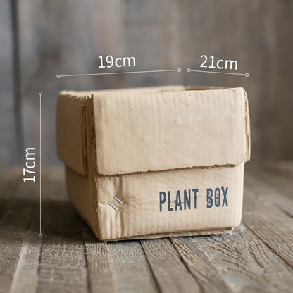 A grey cement flowerpot with a folded paper box design, shown with a drainage hole in its base.