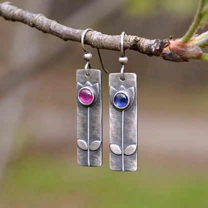 A pair of red sapphire earrings with an antique electroplated finish and a geometric elliptical shape on a plain background.