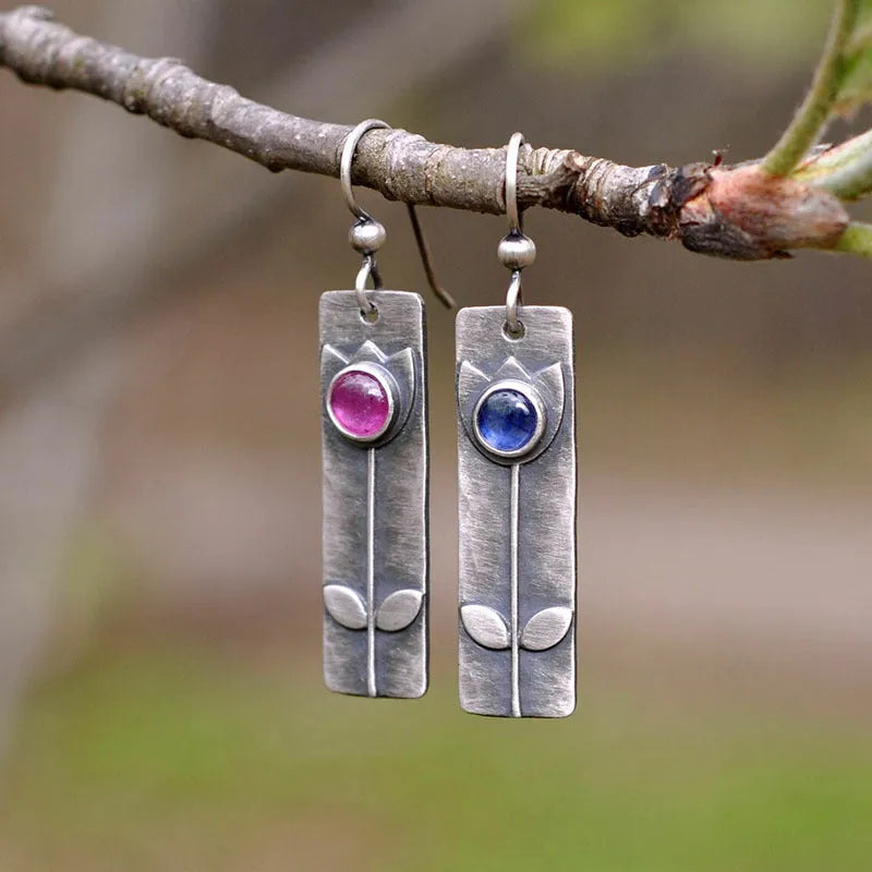 A pair of antique-finish geometric earrings with a red sapphire stone in an elliptical silver-tone setting.
