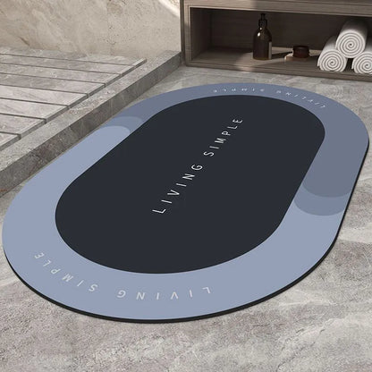 Oval grey bath mat with non-slip rubber bottom on a tiled floor, showing absorbent fabric surface