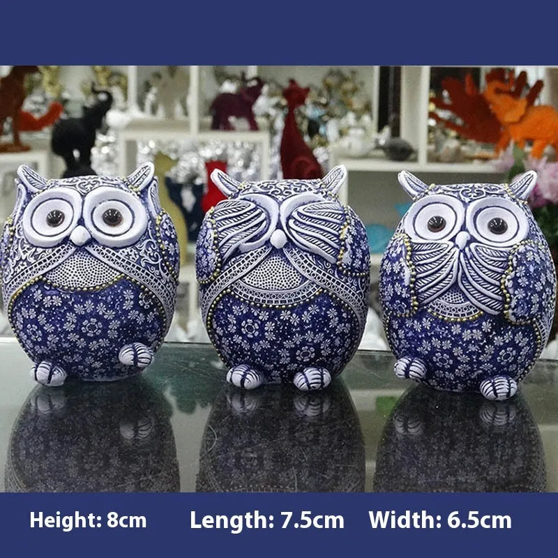 Three blue and white owl resin ornaments with hand-painted pastoral design on wooden surface