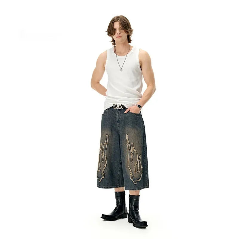 Men's black cropped denim shorts with a red and yellow flame embroidery patch on the leg.