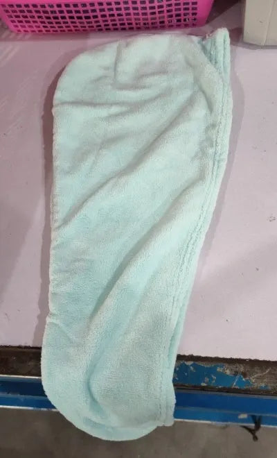 A woman wearing a sky blue microfiber hair dryer cap, with wet hair tucked inside, showing the towel's wrap-around design.