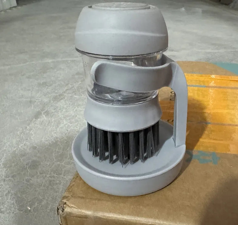 Grey multifunctional kitchen cleaning brush with automatic liquid adding and a scraper edge.