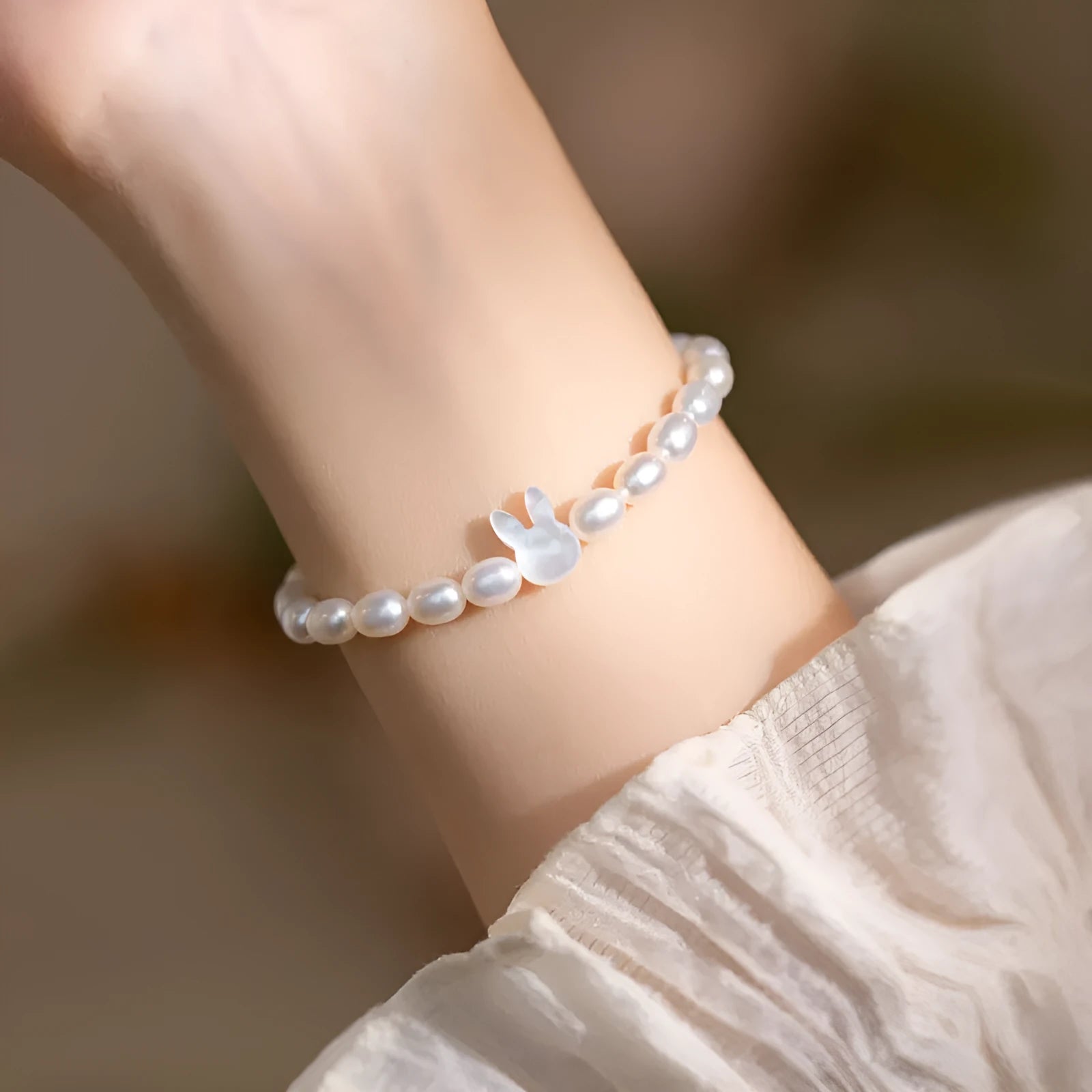 White pearl elastic bracelet with small rice-shaped beads and silver rabbit charm on wrist