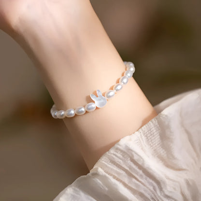 White pearl elastic bracelet with small rice-shaped beads and silver rabbit charm on wrist