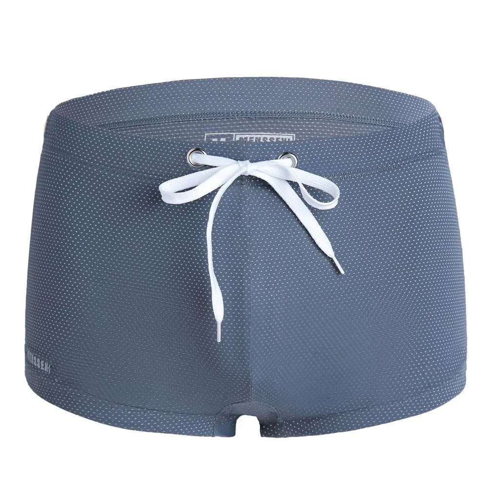 Men's low waist swim trunks in stretch nylon on a man, showing elastic waistband and boxer-style cut.
