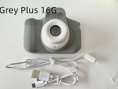 X2 HD mini digital camera for kids in silicone case with lanyard, shown capturing photo on 2-inch screen.