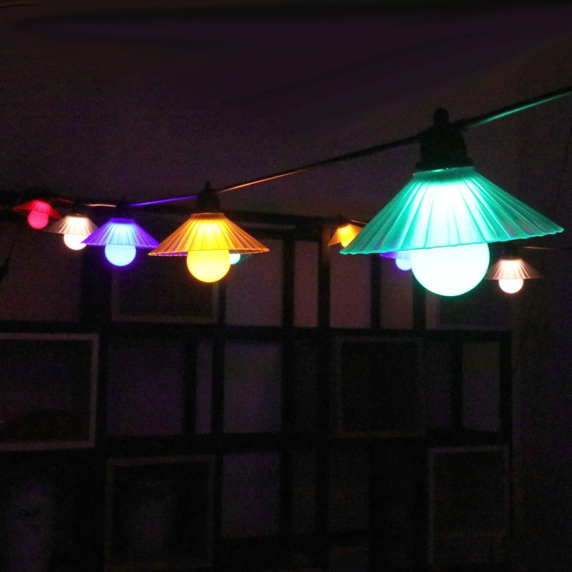 Outdoor LED string lights with white flower-shaped globes, shown illuminating a garden patio at dusk.
