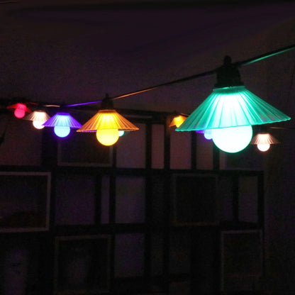Outdoor LED string lights with white flower-shaped globes, shown illuminating a garden patio at dusk.