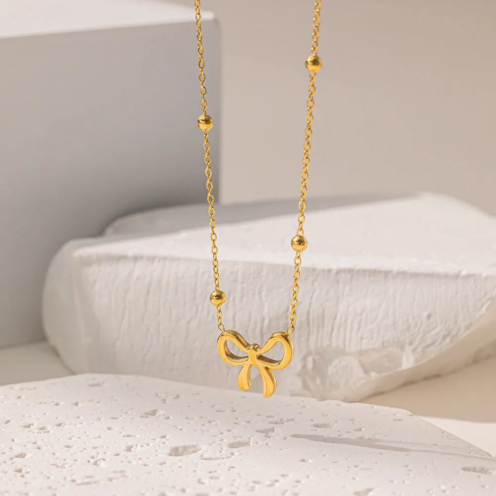 Gold adjustable bow necklace on a cross-link chain, showing the detailed pendant and clasp.
