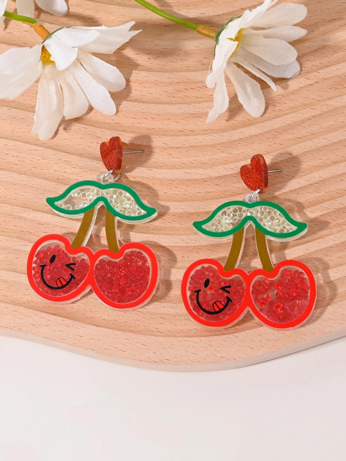 A pair of colourful acrylic earrings shaped like a strawberry and a cherry on a woman's ear.