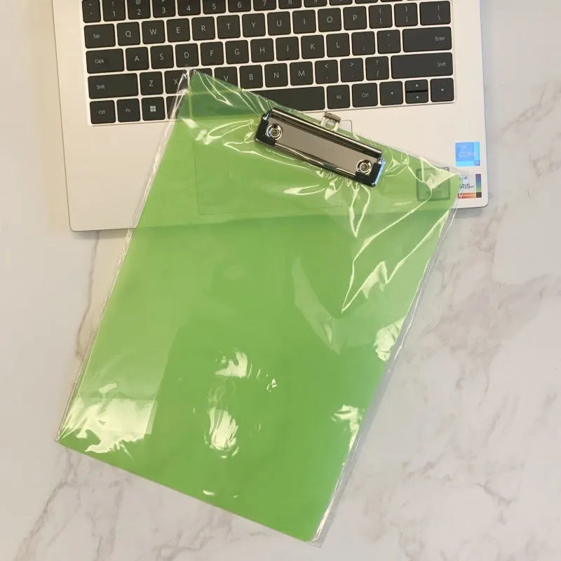 Transparent A4 plastic plate holder with metal clip, holding white paper, on a desk.
