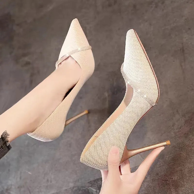 Gold women's stiletto high heels with pointed toe on a plain background.