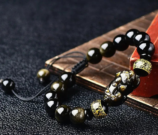 Handmade golden obsidian Pi Xiu bracelet with Chinese zodiac design on wrist.