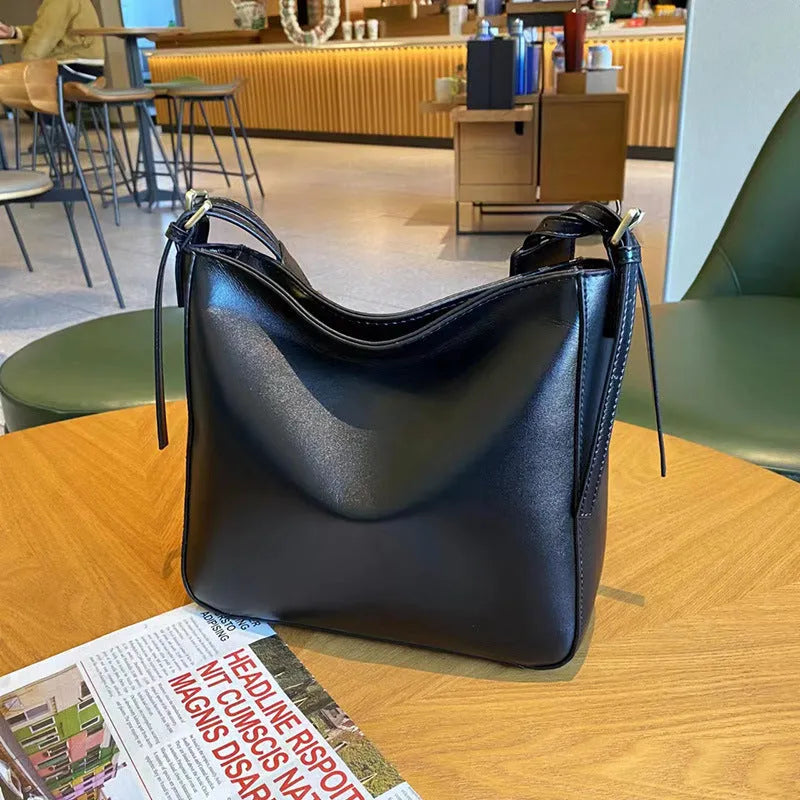 Women's black genuine leather shoulder messenger bag showing structured square shape and single strap.