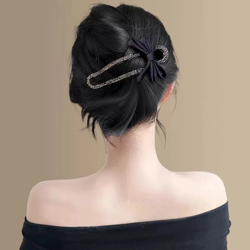A black crystal bow on a clear 11.5cm long acrylic banana hair clip with bobby pin back.
