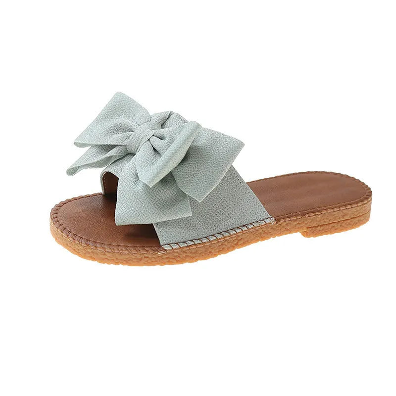 Women's beige suede slip-on sandals with a bow detail and soft rubber flat sole.