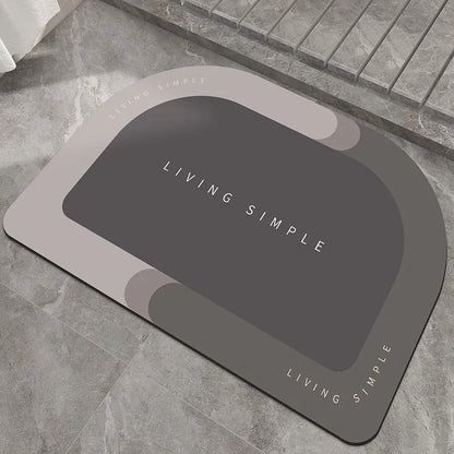 Oval grey bath mat with non-slip rubber bottom on a tiled floor, showing absorbent fabric surface