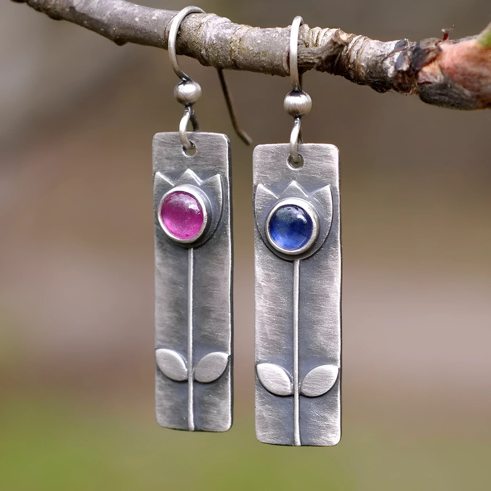 A pair of red sapphire earrings with an antique electroplated finish and a geometric elliptical shape on a plain background.
