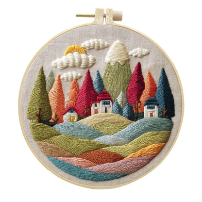 Complete DIY embroidery kit with 15cm bamboo frame, pre-printed landscape fabric, threads, and needles laid out.