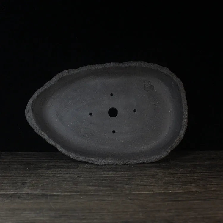 Handmade purple clay flower pot in a creative shape on a floor.