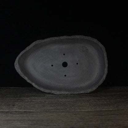 Handmade purple clay flower pot in a creative shape on a floor.