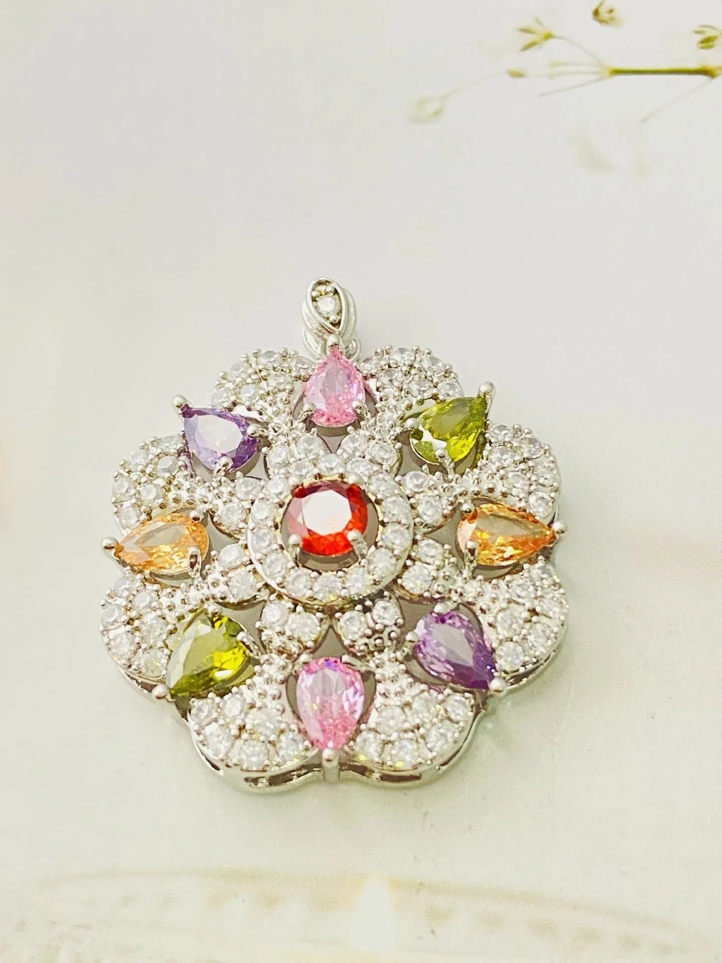 Close-up of a women's flower-shaped pendant necklace with a colourful zircon stone in a choice of gold, champagne gold, or platinum colour finishes.