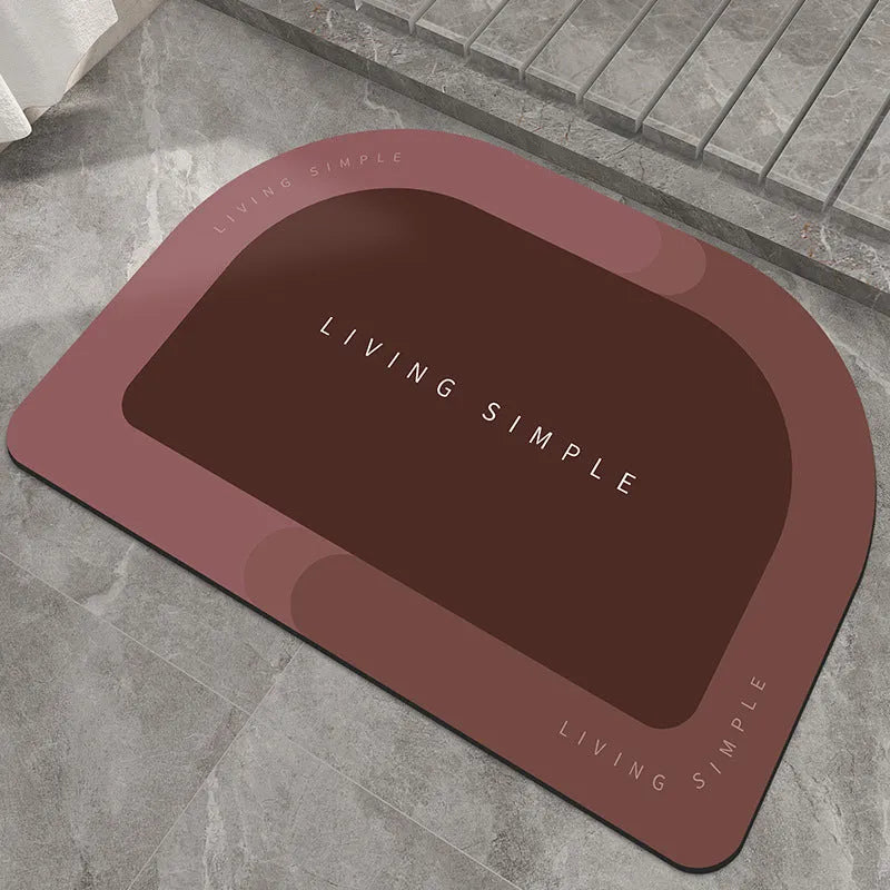 Oval grey bath mat with non-slip rubber bottom on a tiled floor, showing absorbent fabric surface