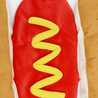 Small dog wearing a humorous stuffed hot dog costume suit in a winter setting.